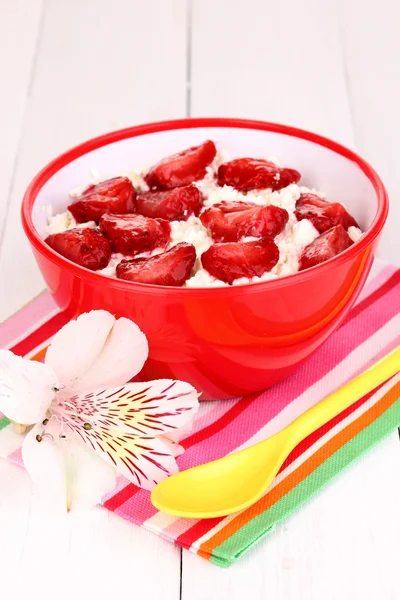 Twaróg w czerwony bowl z pokrojone truskawki na biały drewniany stół — Zdjęcie stockowe