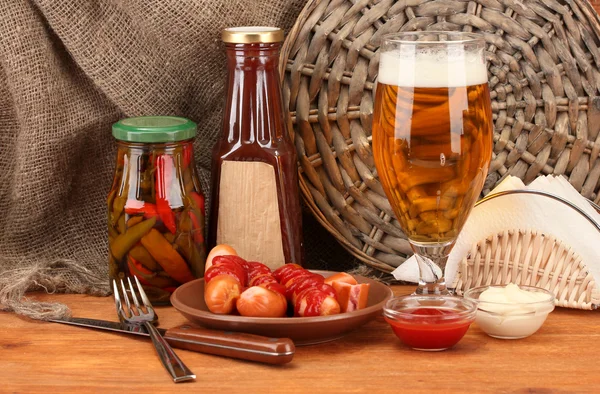 Bière et saucisses grillées sur table en bois sur fond de sac — Photo