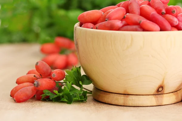 Rijpe barberries in houten kom met groene bladeren, op tafel — Stockfoto