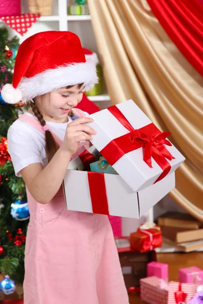 A little girl opens a gift in festively decorated room Stock Picture