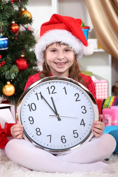 Beautiful little girl with clock in anticipation of New Year in festively decorated room Royalty Free Stock Photos