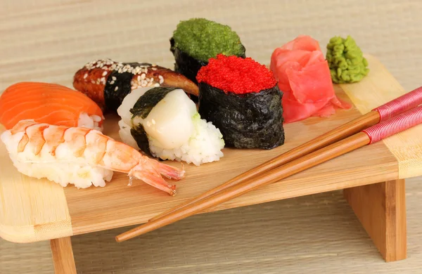 Köstliches Sushi auf Holzbrett auf Bambusmatte serviert — Stockfoto