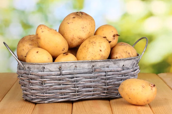 Reife Kartoffeln auf Korb auf Holztisch vor natürlichem Hintergrund — Stockfoto