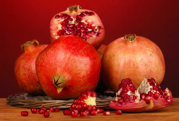Zralé granátová jablka na proutěný stojan na červeném pozadí — Stock fotografie