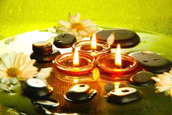 Spa stones with flowers and candles in water on plate — Stock Photo, Image