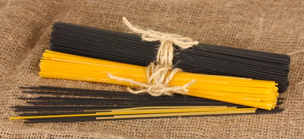 Espaguete preto e amarelo sobre fundo de pano de saco — Fotografia de Stock