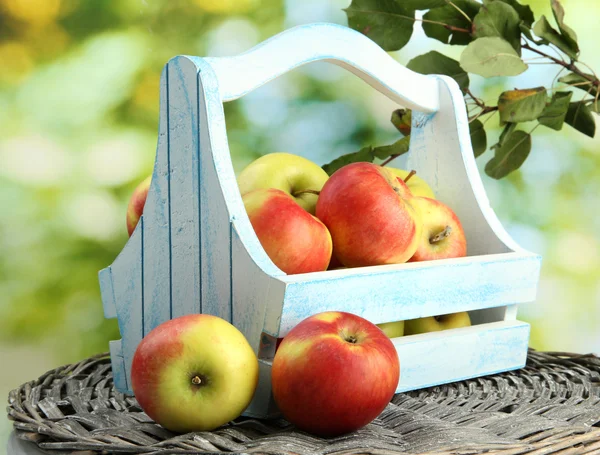 Saftiga äpplen med blad i trä korg, på grön bakgrund — Stockfoto