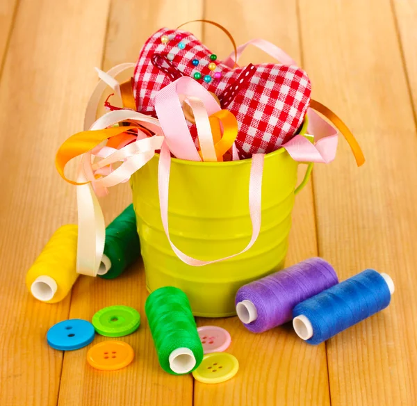 Color bucket with multicolor ribbons and thread on wooden background — Stock Photo, Image