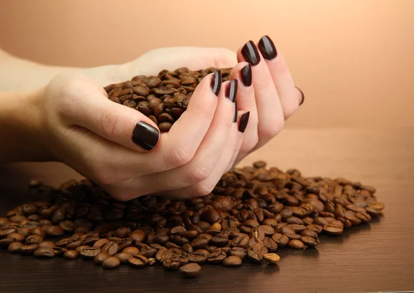 Female hands with coffee beans, on brown background — Stock Photo, Image