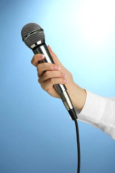 Main féminine avec microphone, sur fond bleu — Photo