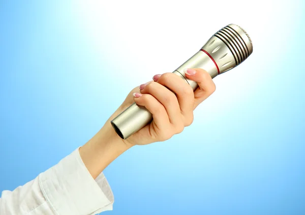 Mano femenina con micrófono, sobre fondo azul — Foto de Stock
