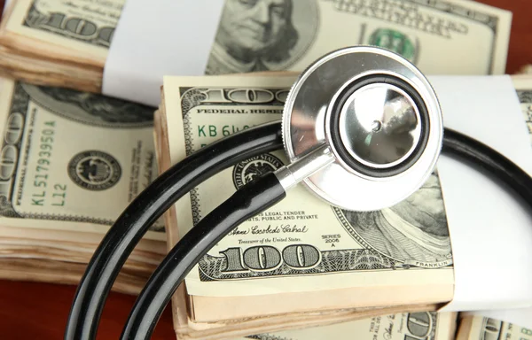 Healthcare cost concept: stethoscope and dollars on wooden background — Stock Photo, Image