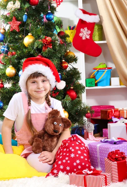 Petite fille au chapeau de Père Noël près du sapin de Noël dans une chambre décorée de façon festive — Photo