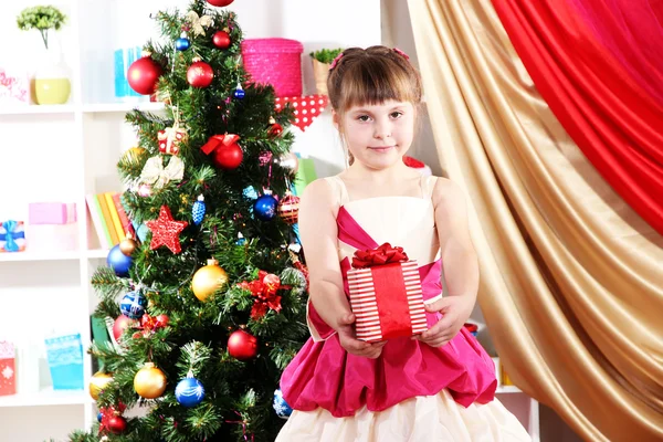 Menina bonita em vestido de férias com presente em suas mãos no quarto festivamente decorado — Fotografia de Stock