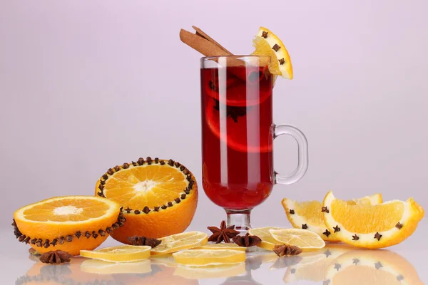 Fragrant mulled wine in glass with spices and oranges around on purple background — Stock Photo, Image