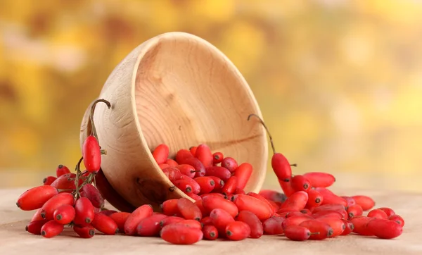 Ripe barberries in wooden bowl, on table, on yellow background — Stock Photo, Image