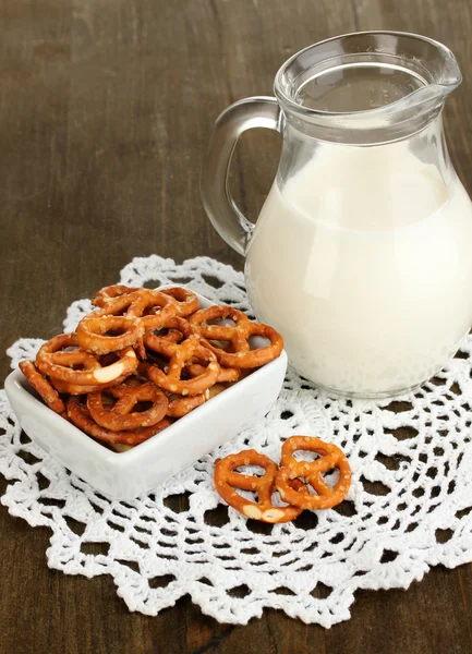 Tasty pretzels in white bowl and milk jug on wooden table close-up — Stock Photo, Image