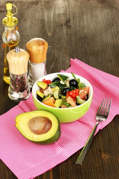 Tasty avocado salad in bowl surrounded by spices on wooden table close-up