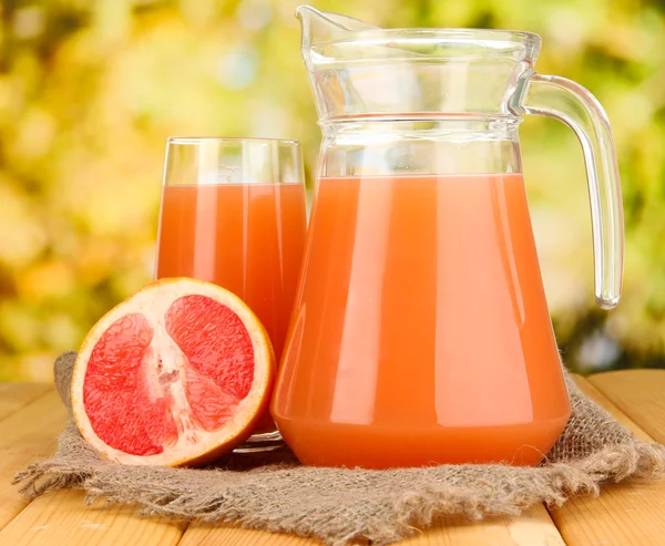 Full glass and jug of grapefruit juice and grapefruits on wooden table outdoor — Stock Photo, Image