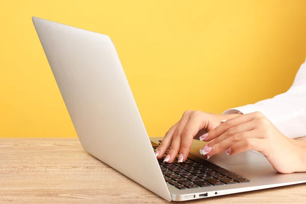 Mani di donna d'affari digitando sul computer portatile, su sfondo giallo primo piano — Foto Stock