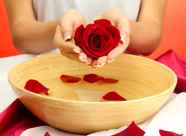 Woman hands with wooden bowl of water with petals, on red background — Stock Photo, Image