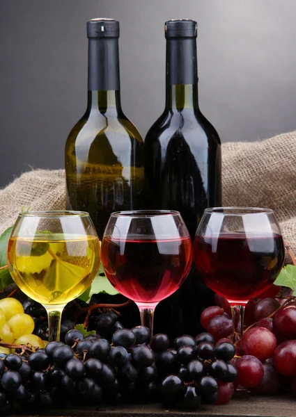 Botellas y vasos de vino y uvas sobre fondo gris — Foto de Stock