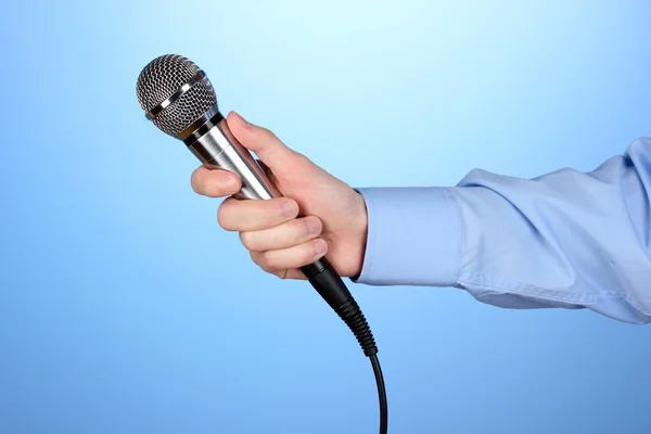 Männliche Hand mit Mikrofon auf blauem Hintergrund — Stockfoto