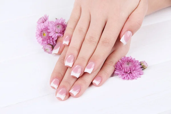 Woman hands with french manicure and flowers on white wooden background Stock Photo