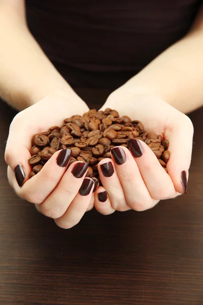 Manos femeninas con granos de café, sobre fondo de madera — Foto de Stock