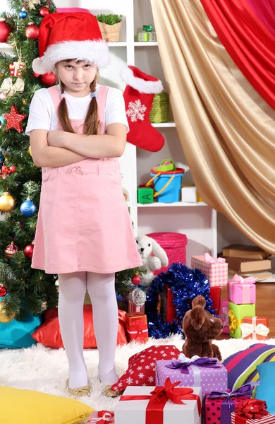 Molesto por la niña cerca del árbol de Navidad en la habitación festivamente decorada —  Fotos de Stock
