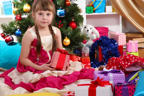 Mooi meisje in vakantie jurk met cadeau in hun handen in feestelijk versierde kamer — Stockfoto