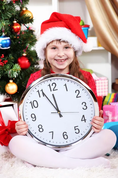 Красивая маленькая девочка с часами в преддверии Нового года в празднично оформленном помещении — стоковое фото