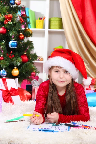 Belle petite fille écrit une lettre au Père Noël dans une chambre décorée de façon festive — Photo