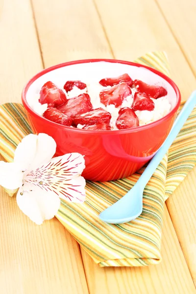 Hüttenkäse in roter Schüssel mit Erdbeeren in Scheiben auf Holztisch — Stockfoto
