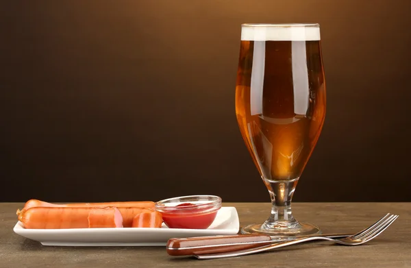 Bier und Grillwürste auf Holztisch vor braunem Hintergrund — Stockfoto