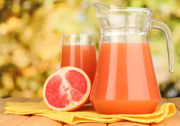Full glass and jug of grapefruit juice and grapefruits on wooden table outdoor — Stock Photo, Image