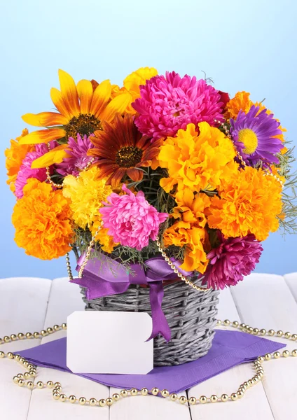 Beautiful bouquet of bright flowers with paper note on wooden table on blue background — Stock Photo, Image