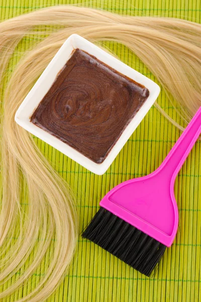 Tinte para el cabello en un tazón y cepillo para la coloración del cabello en una esterilla de bambú verde, primer plano — Foto de Stock