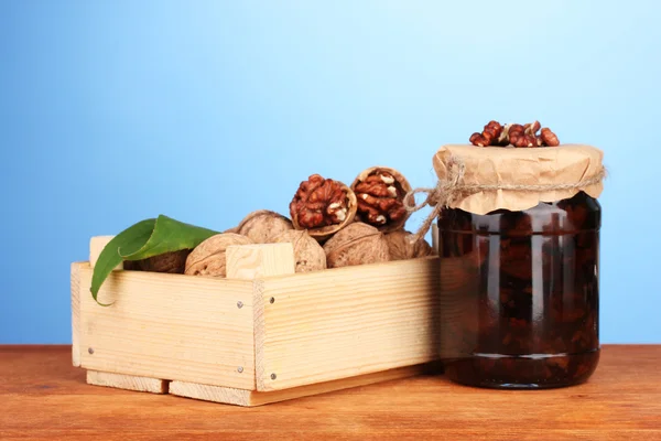 Jam-jar of walnuts and wooden box on blue background — Stock Photo, Image