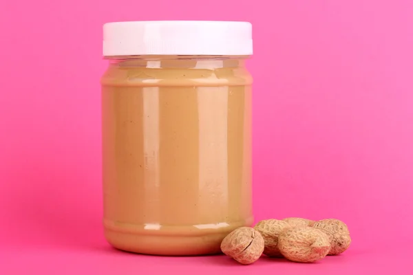 Delicious peanut butter in jar of peanut near on pink background — Stock Photo, Image