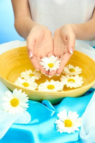 Manos de mujer con cuenco de madera de agua con flores, sobre fondo azul — Foto de Stock