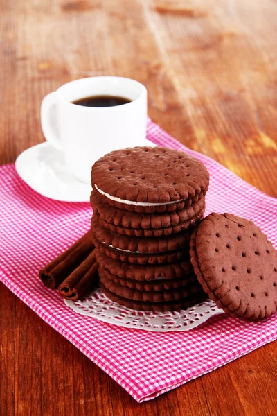 Schokoladenkekse mit cremiger Schicht und Tasse Kaffee auf Holztisch in Großaufnahme — Stockfoto