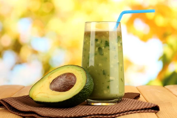 Nützliche frische Avocado und halbe Avocado auf Holztisch vor natürlichem Hintergrund — Stockfoto