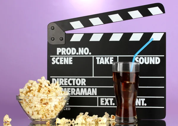 Movie clapperboard, cola and popcorn on purple background — Stock Photo, Image