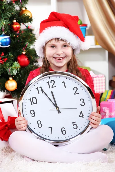 Beautiful little girl with clock in anticipation of New Year in festively decorated room Royalty Free Stock Images