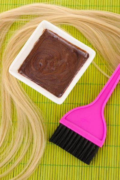 Hair dye in bowl and brush for hair coloring on green bamboo mat, close-up Stock Picture