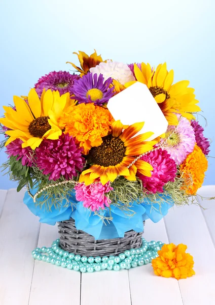 Bellissimo bouquet di fiori luminosi con nota di carta su tavolo di legno su sfondo blu — Foto Stock