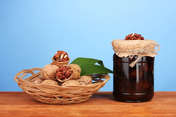 Mermelada-tarro de nueces sobre mesa de madera y una cesta con nueces sobre fondo azul — Foto de Stock