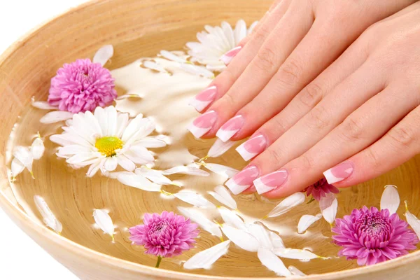 Manos de mujer con manicura francesa y flores en tazón de bambú con agua — Foto de Stock