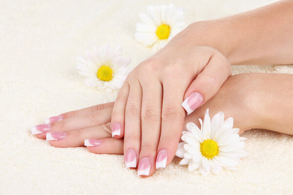 Woman hands with french manicure and flowers on towel
